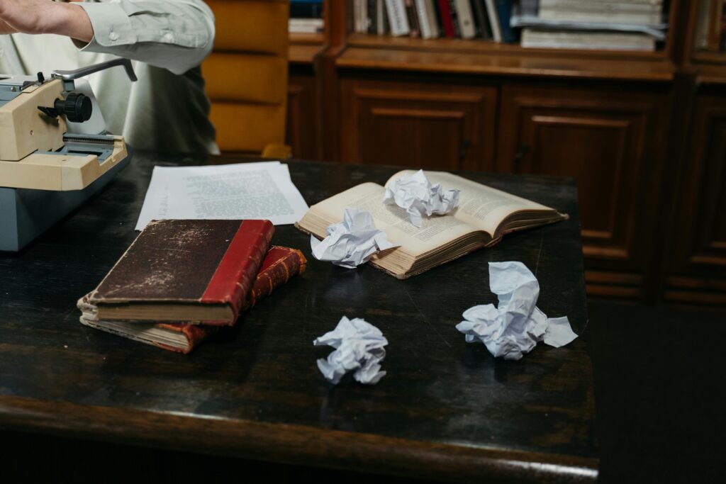 A cozy workspace with typewriter, open books, and crumpled papers on a wooden desk, perfect for creative inspiration.
