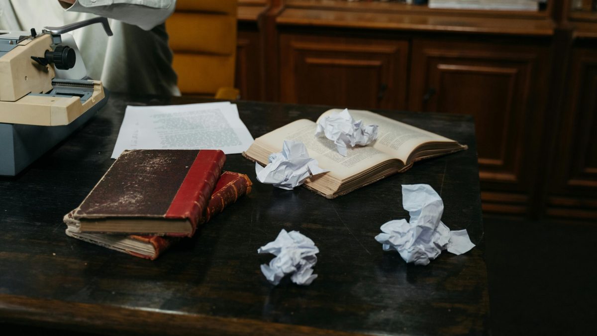 A cozy workspace with typewriter, open books, and crumpled papers on a wooden desk, perfect for creative inspiration.